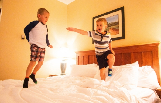 Two kids play on the bed at Rodd Hotel & Resorts.